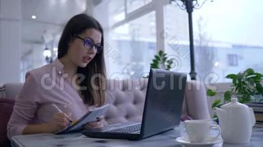 远程<strong>学习</strong>，年轻女子在笔记本电脑上进行在线<strong>交流</strong>，并在咖啡馆的餐桌上展示笔记本